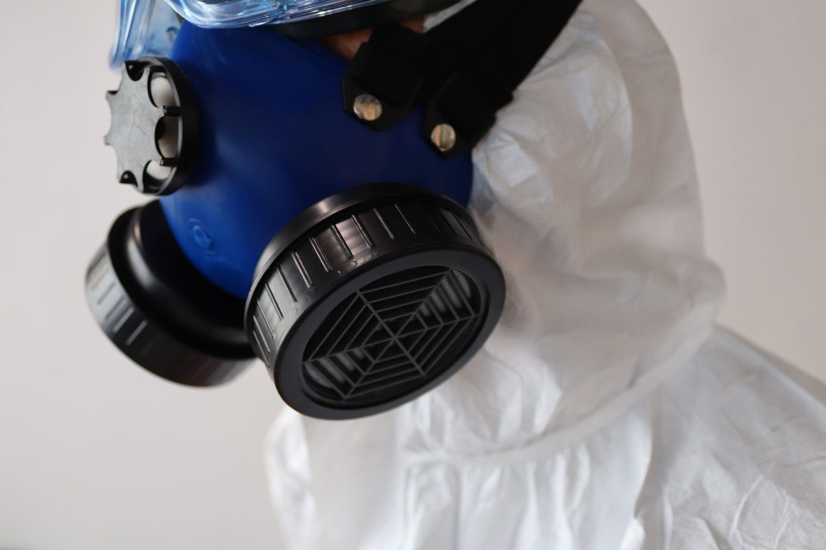 Half-face respirator with filter cartridges, worn with safety goggles and a white disposable coverall