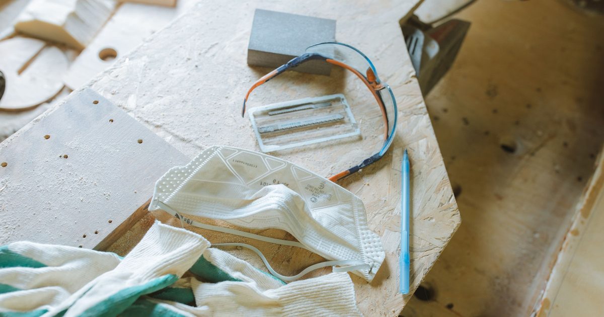 Work gloves, a disposable dust mask and safety glasses on a dusty workbench