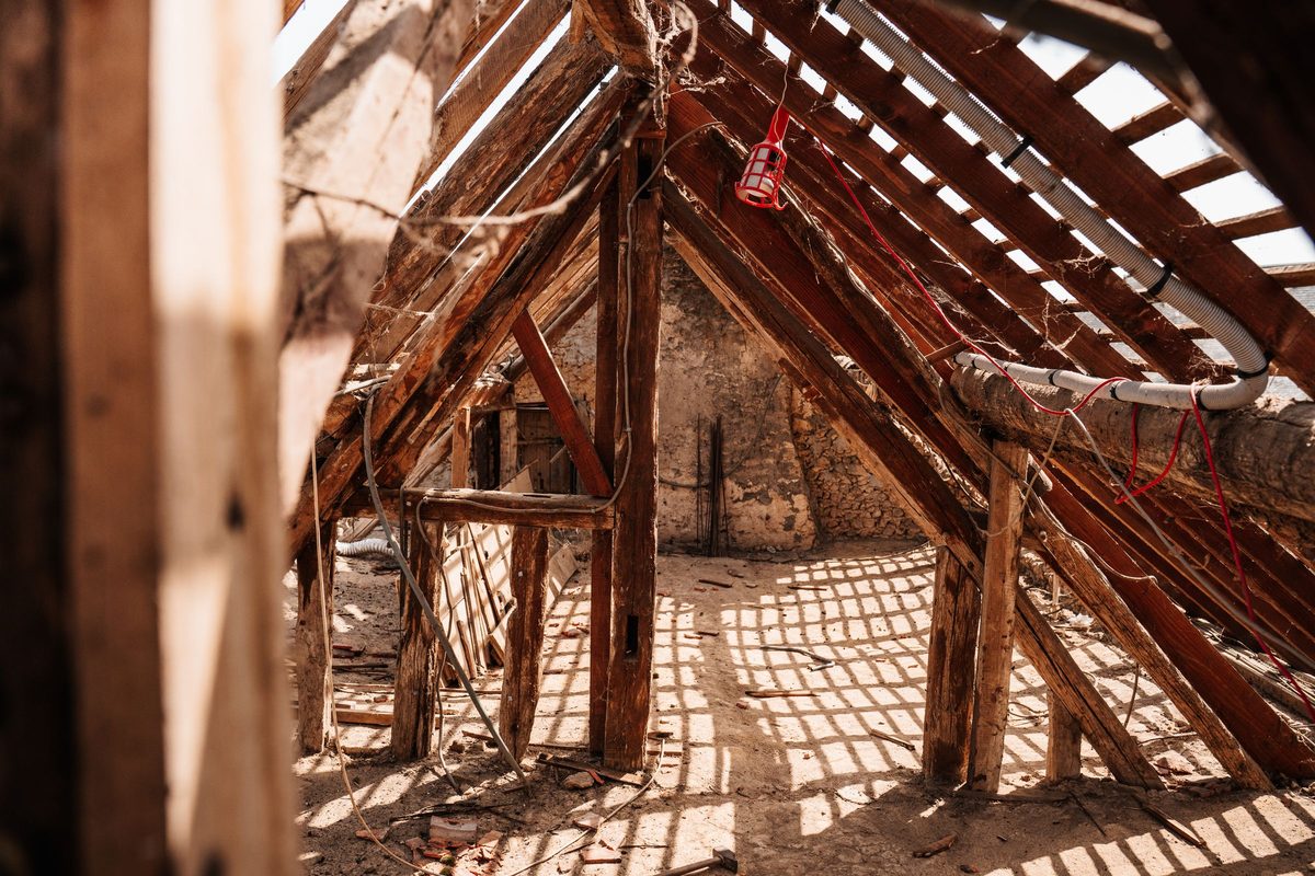 Unfinished attic with wooden rafters and daylight showing through gaps in the roof