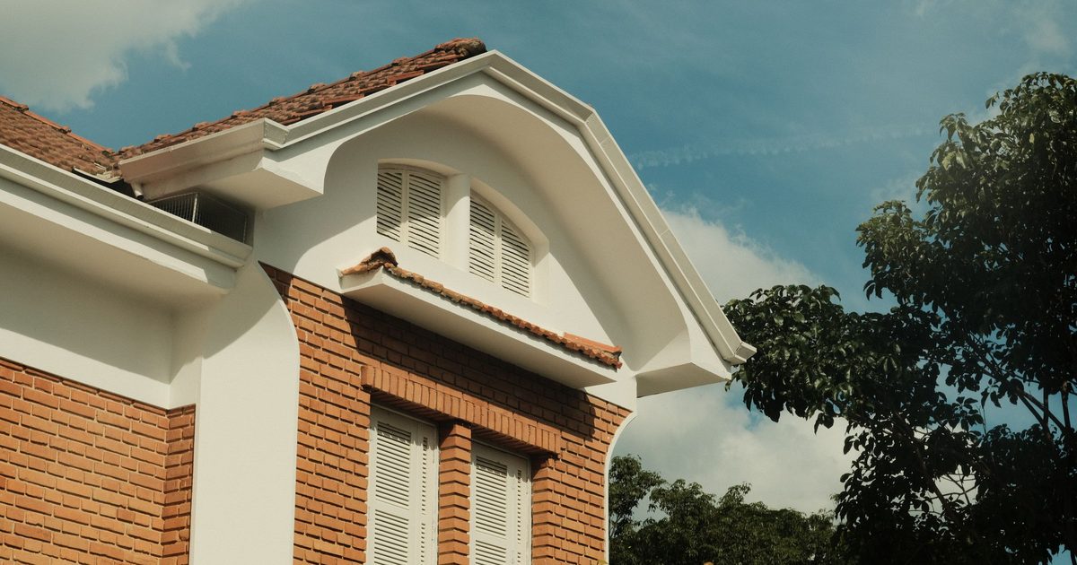 Brick house with white louvered shutters and a metal grille under the eaves