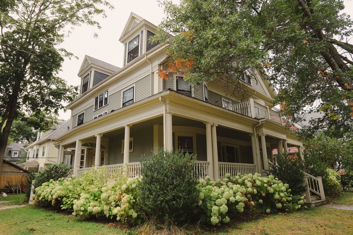 Older two-story house with a wraparound porch under large shade trees